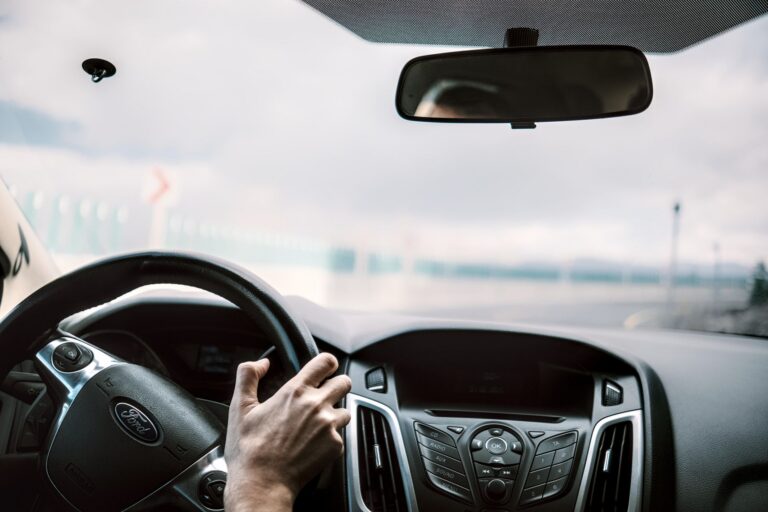 Mâinile unui șofer pe volan, conducând calm pe o autostradă într-o zi senină
