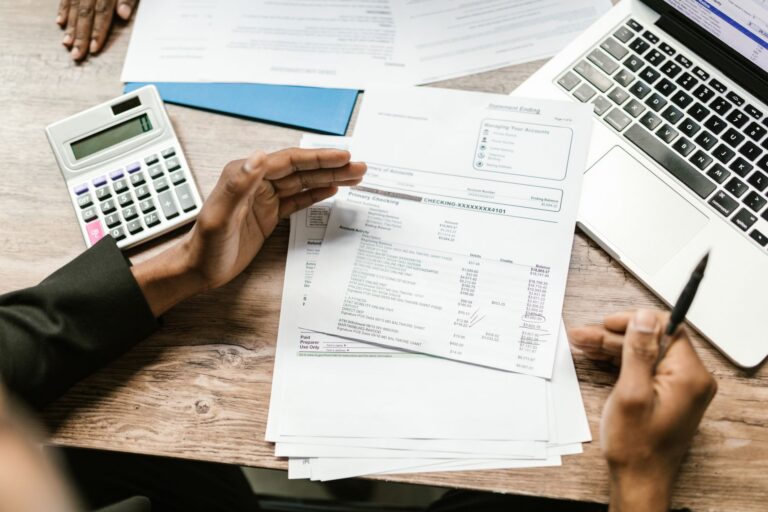Laptop cu un tabel de buget deschis pe ecran, lângă un calculator și o agendă cu notițe